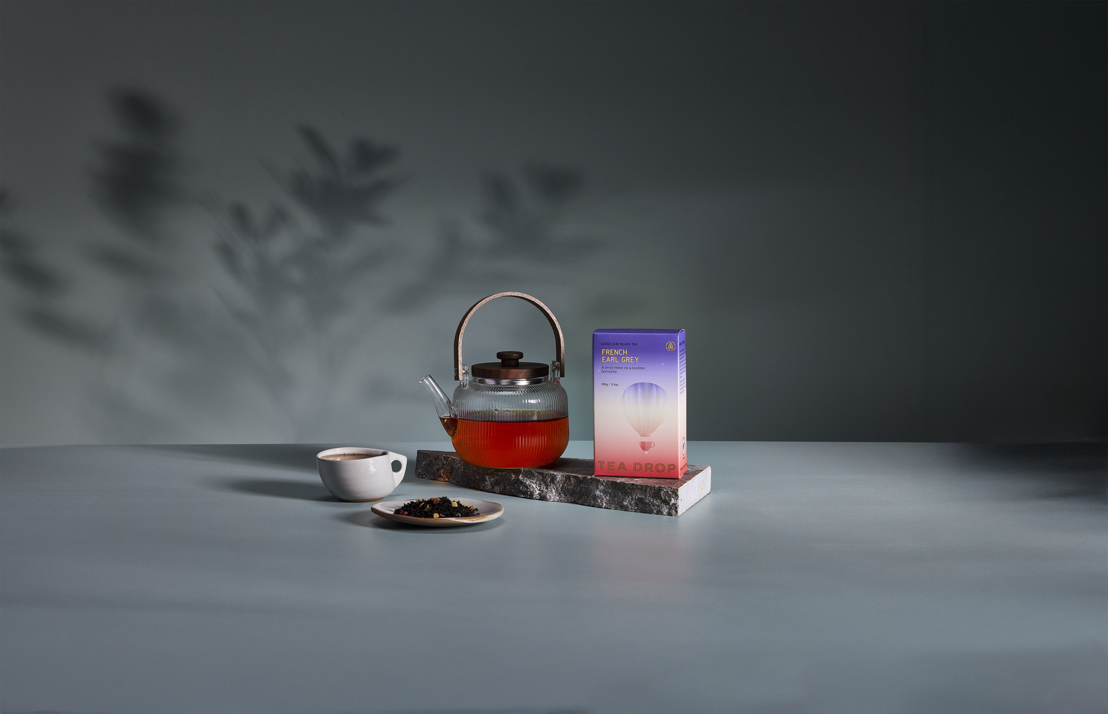 Glass teapot of freshly brewed tea beside a Tea Drop pack